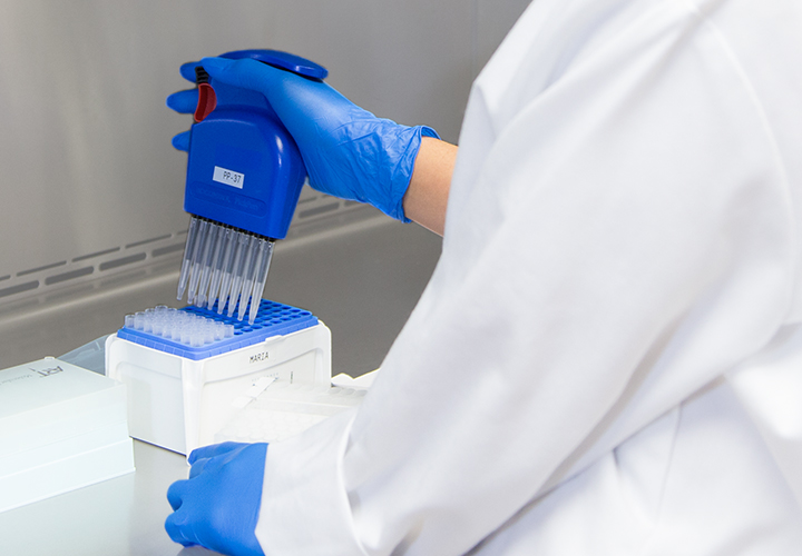 Lab technician using pipette with testing equipment.