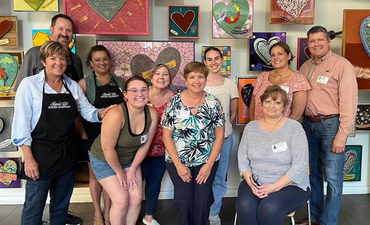 Group of adults posing together in front of colorful heart artwork.