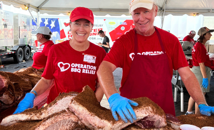 Two volunteers in red shirts serving food at an Operation BBQ Relief event.