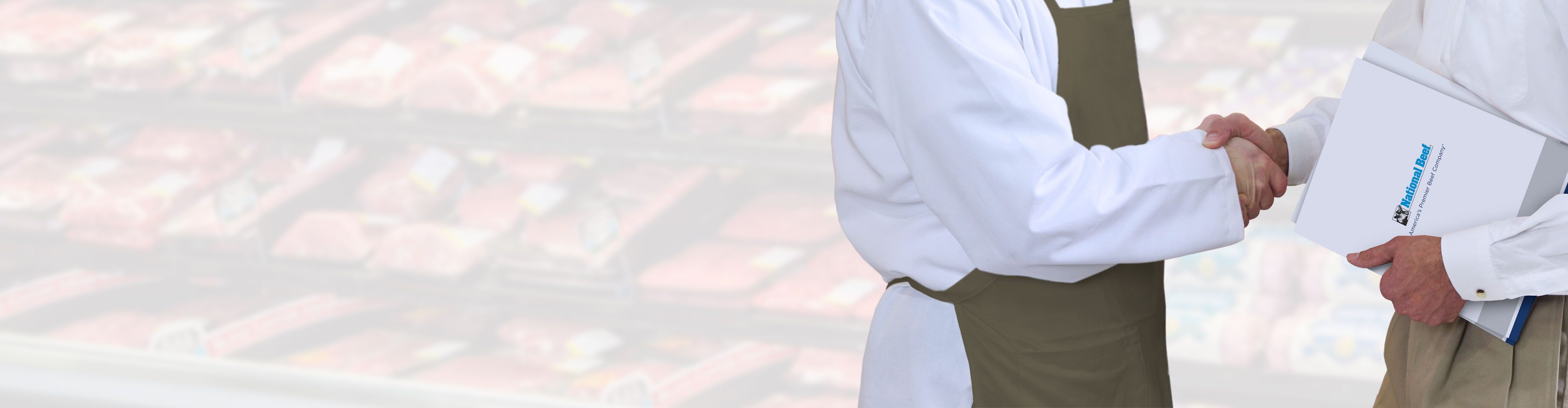 Two people in butcher uniforms shaking hands in front of a meat display