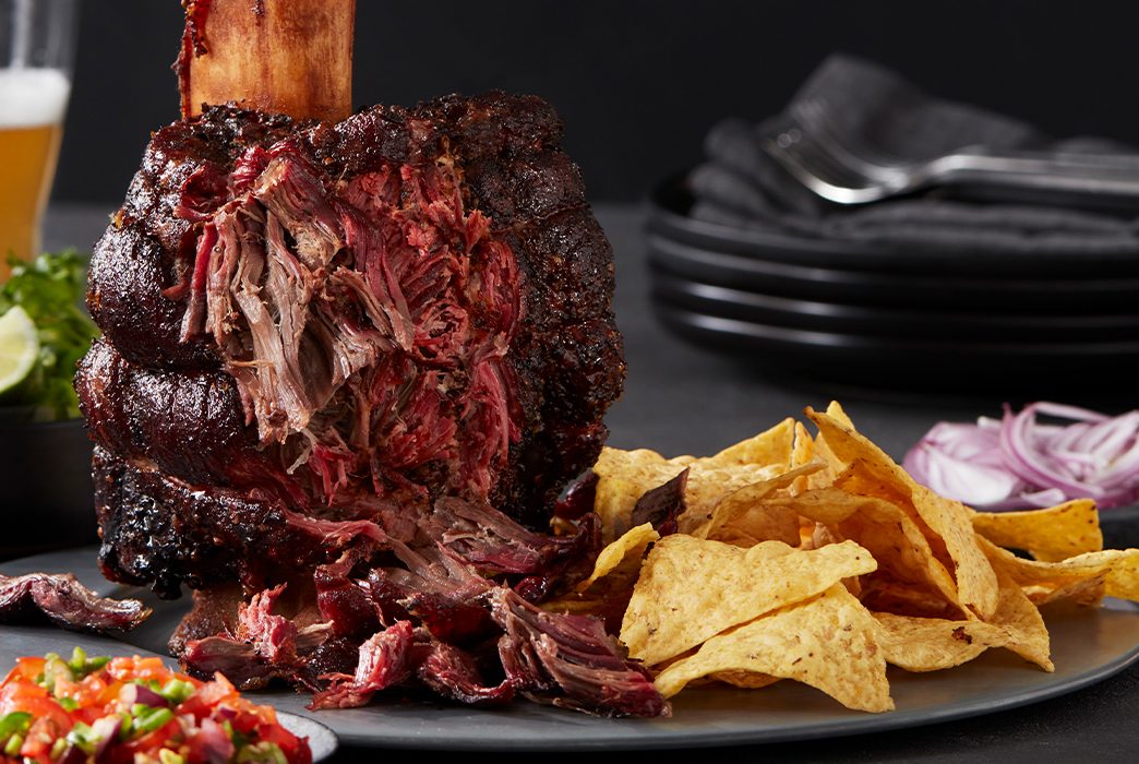 Cooked beef shank pulled apart on a plate with tortilla chips, onions, and salsa.