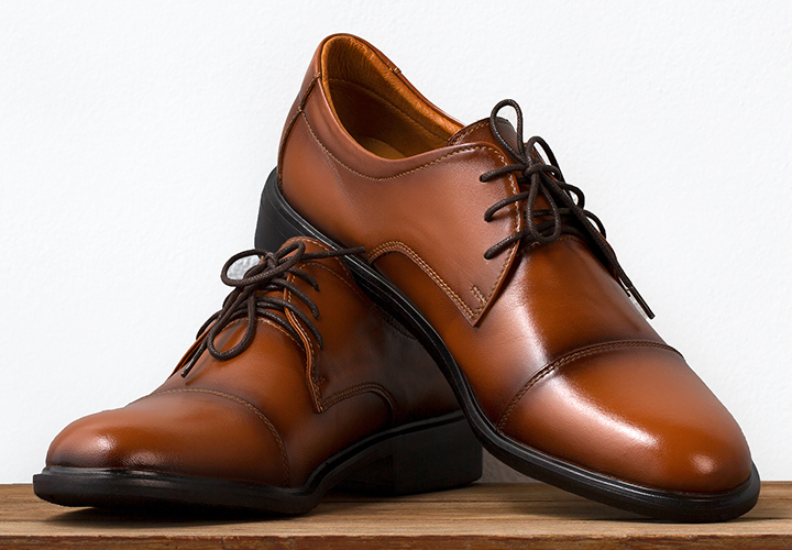 Pair of polished brown leather dress shoes on a light background.