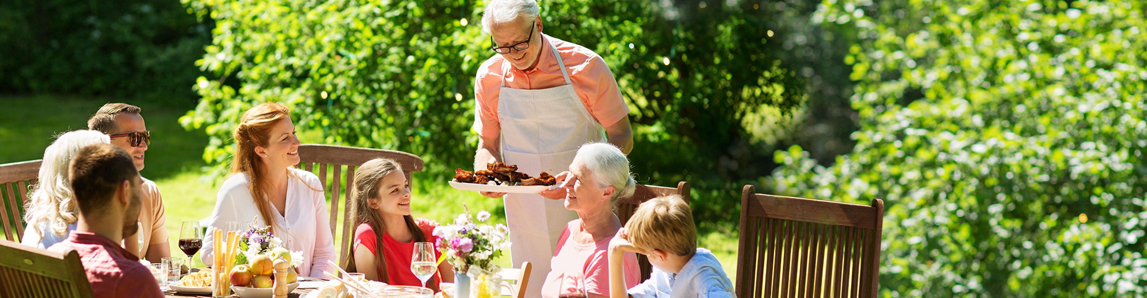 Family enjoying an outdoor meal at a sunny picnic table surrounded by greenery.