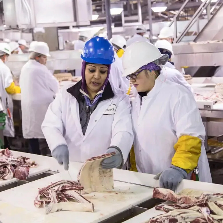 Supervisor training an employee on trimming beef cuts inside a processing plant.