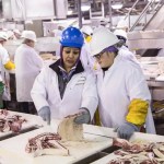 Supervisor training an employee on trimming beef cuts inside a processing plant.