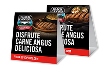 Two Spanish Black Canyon Angus Beef table tents with one with a plated ribeye, the other with a plated strip steak.