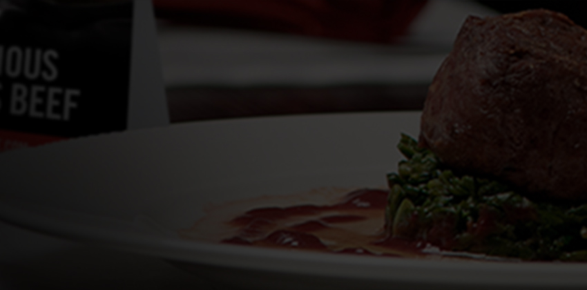Beef medallion on greens with sauce and blurred enjoy delicious angus beef sign in background
