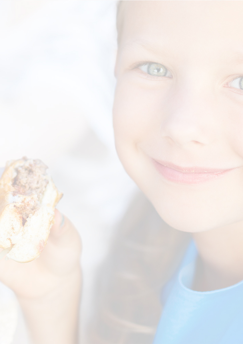 Smiling young girl holding and eating a hamburger outdoors.