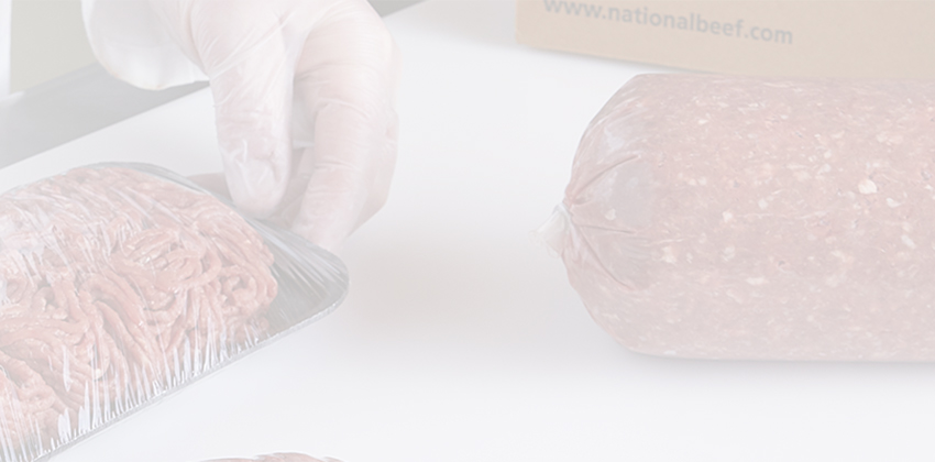 Worker in gloves placing ground beef into a tray next to a large clear-wrapped ground beef chub.