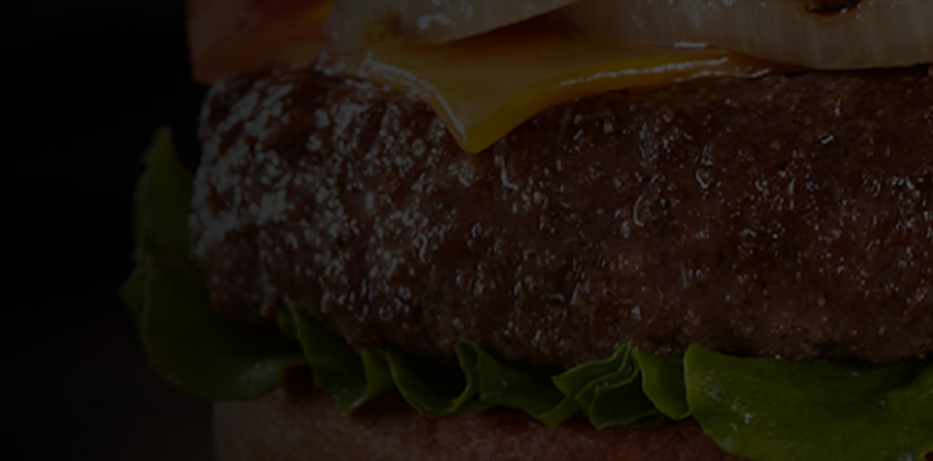 Close-up of a loaded cheeseburger with lettuce, tomato, pickles, onions, and a toasted bun.