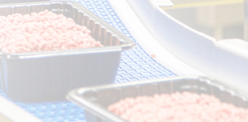 Soft-focus image of multiple trays of ground beef moving along a production line.