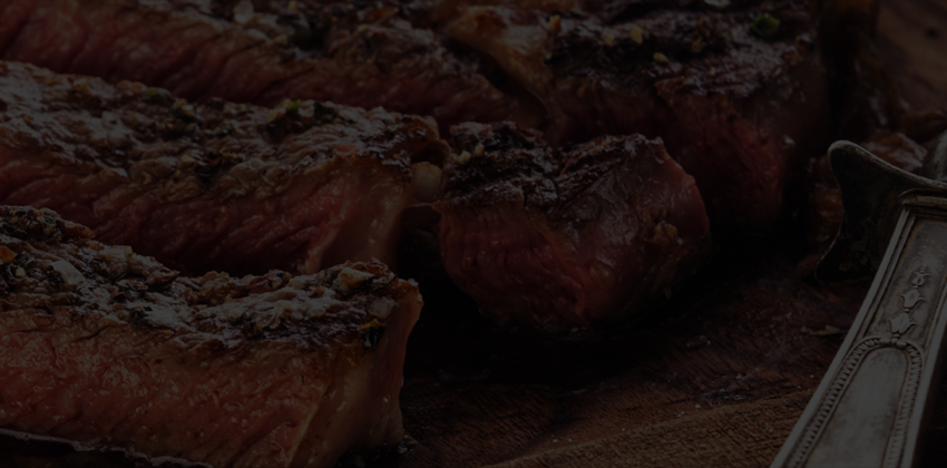 Sliced grilled steak on a wooden board with steak knives