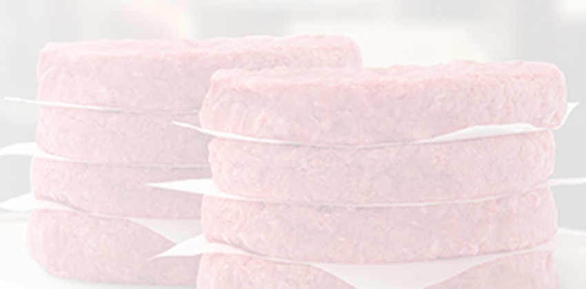 Stacks of raw ground beef patties separated by paper sheets on a wooden board.