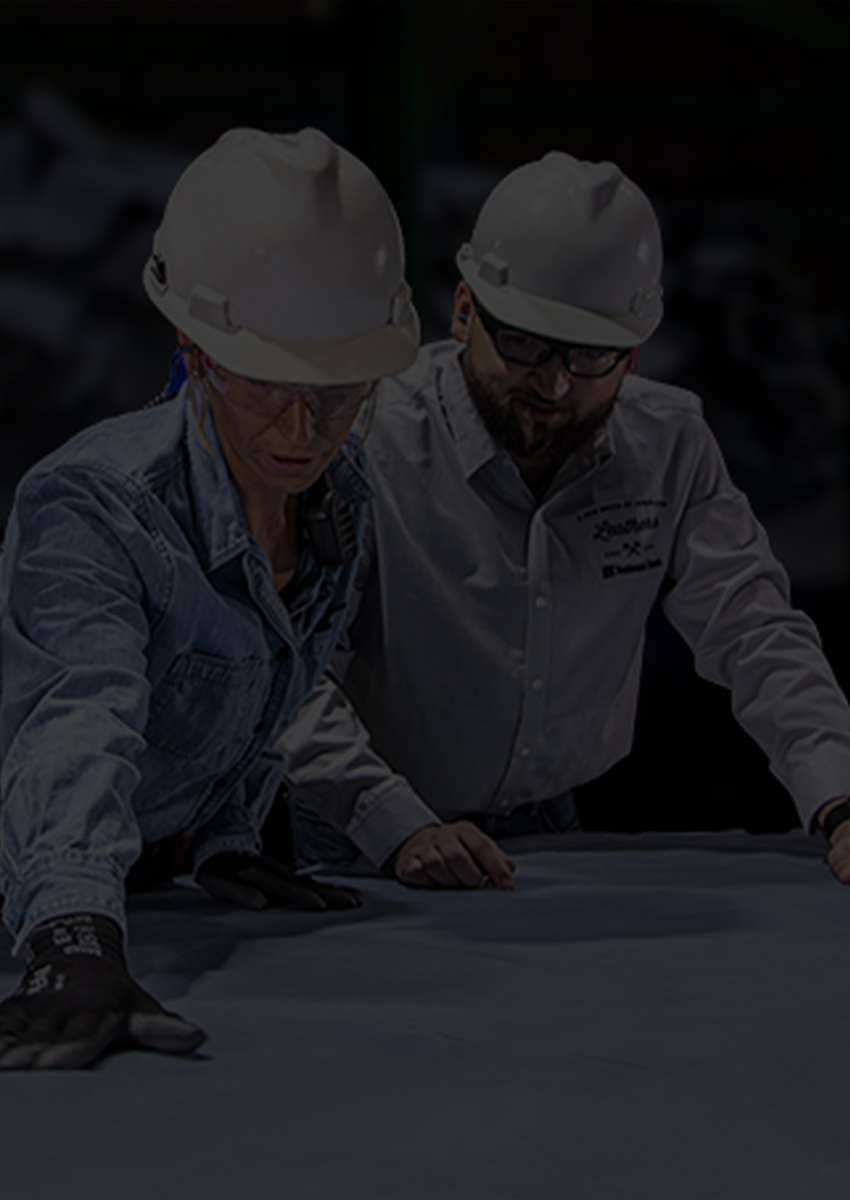 Workers in hard hats inspecting a large sheet of leather in a factory.