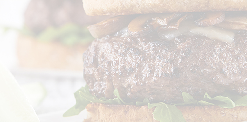 Gourmet beef burger stacked with toppings on bun with pickle spears on the side