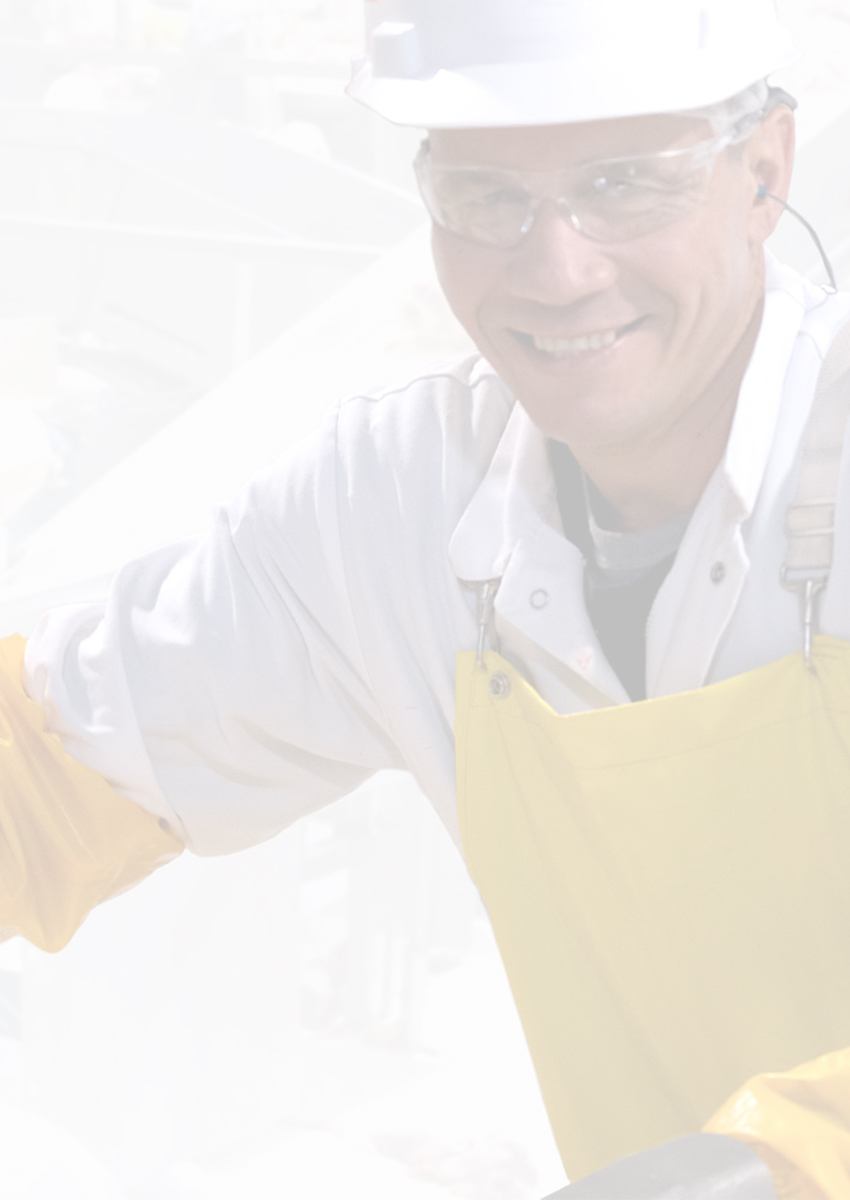 Worker in safety gear smiling while handling a large cut of meat in a meat processing facility.