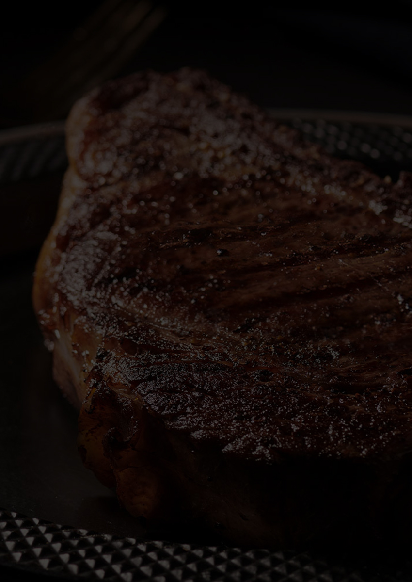 Close-up of a grilled steak on a dark plate with dim lighting.