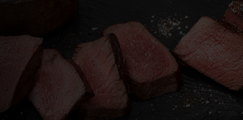 Sliced medium-rare steak arranged on a dark slate surface with coarse salt and pepper