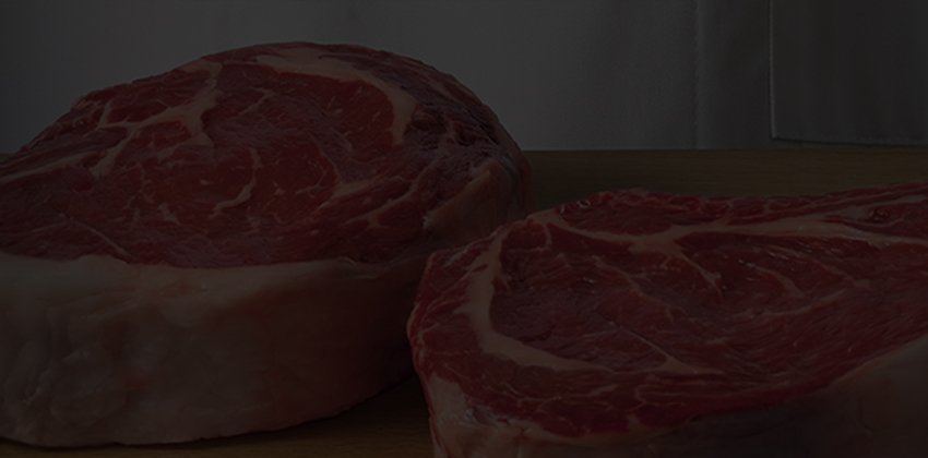 Two thick-cut ribeye steaks on cutting board beside chef, with dark textured background.