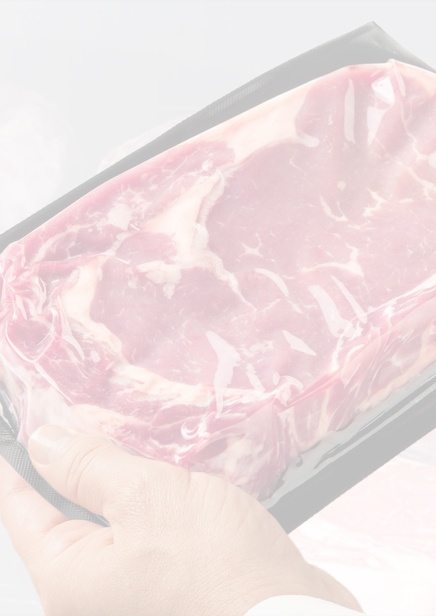 Person holding a vacuum-sealed steak in front of a display case filled with packaged steaks.