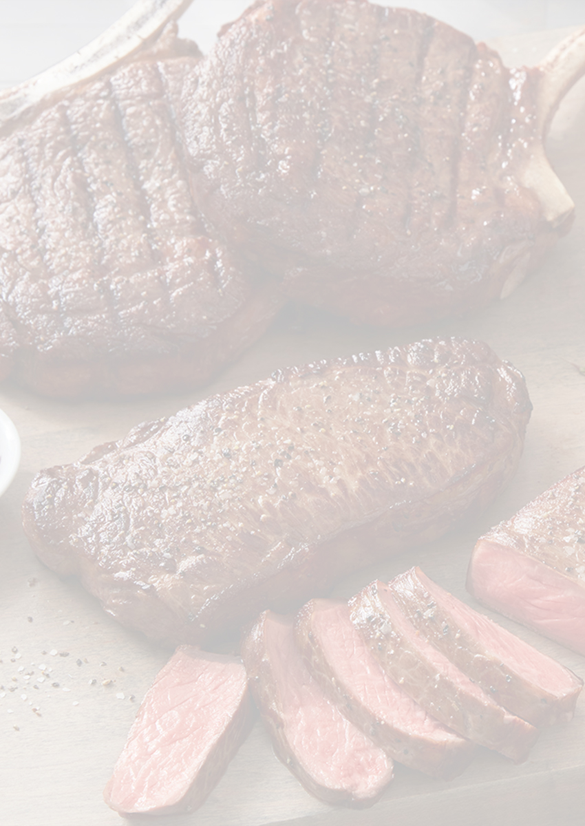 A selection of cooked steaks on a wooden board with condiments and garnishes.