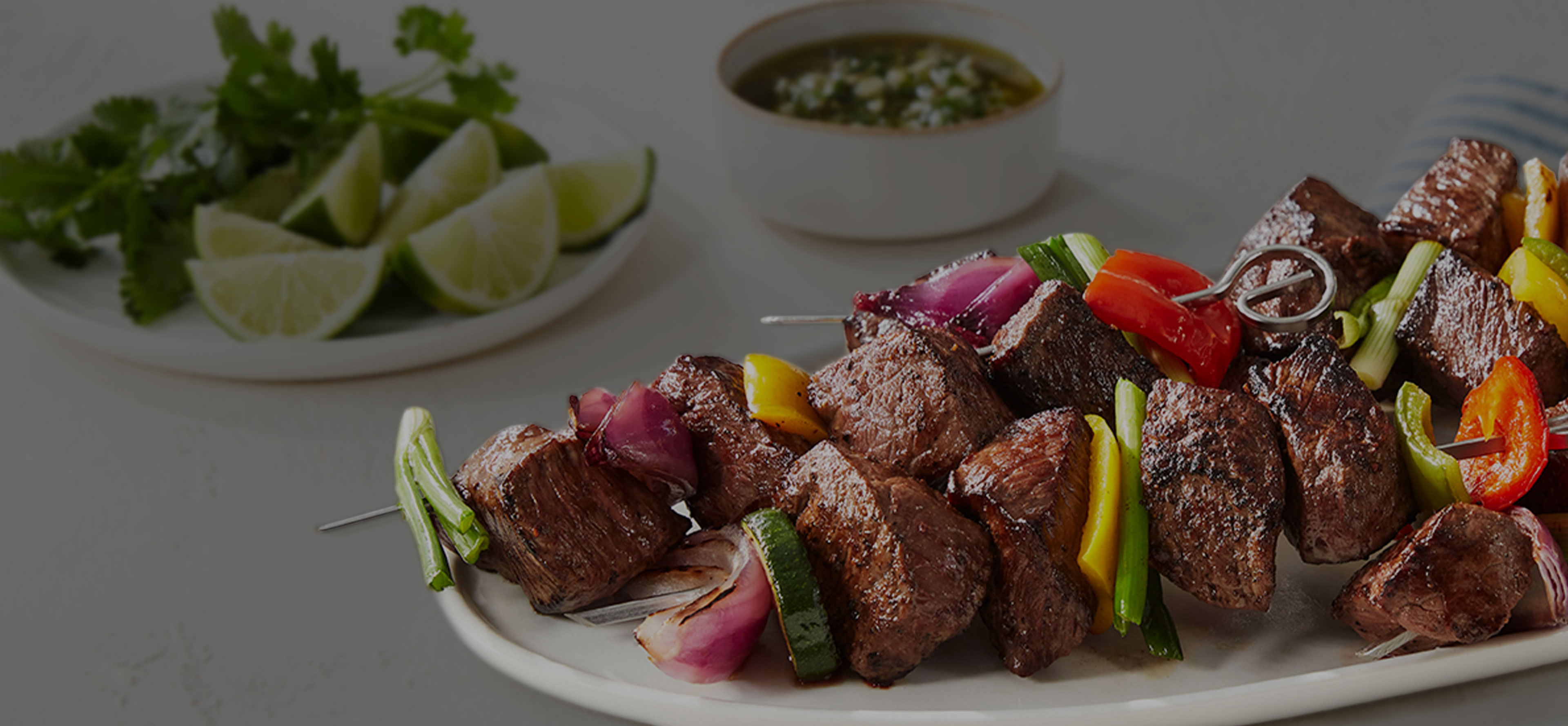 Beef Kebabs on a plate with limes and sauce in the background