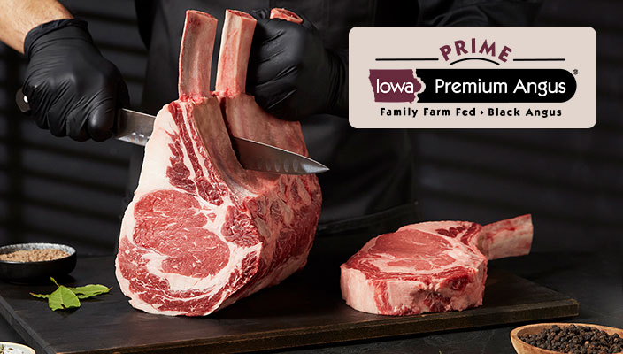 A butcher slicing a prime rib roast on a cutting board  with a ribeye steak lying next to the roast. The Iowa Premium Prime logo is place in the upper right corner.